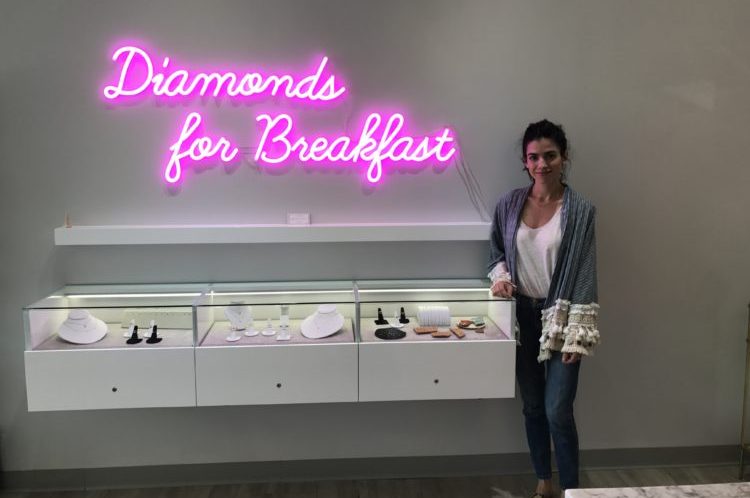 Lucia Mouet Stands Inside Coronado Store by display case and sign "Diamonds For Breakfast"