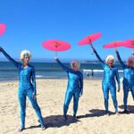 SharkBait Mamas with pink umbrella on beach