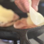 The provolone is placed on the mortadella after it is flipped in the pan.